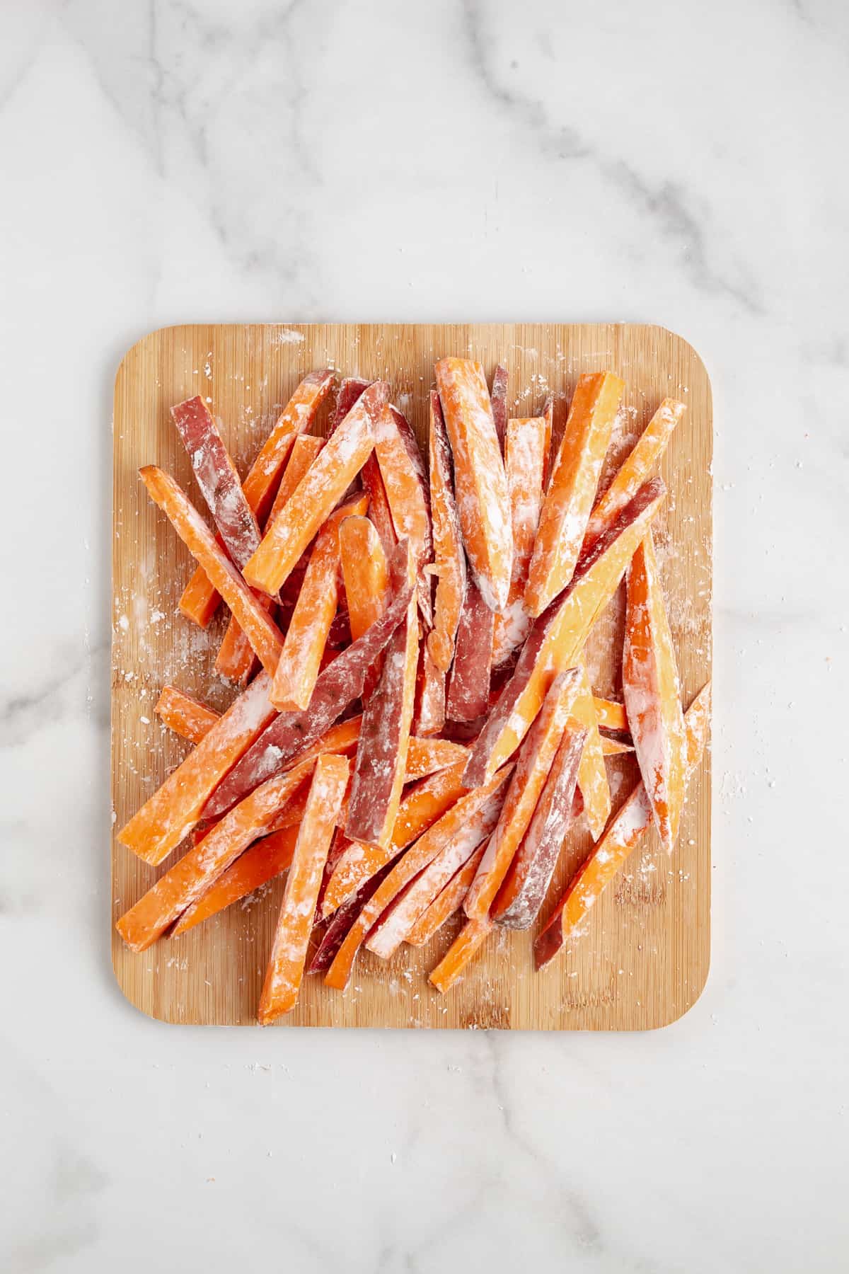 Sweet potato fries tossing with cornstarch on a cutting board.