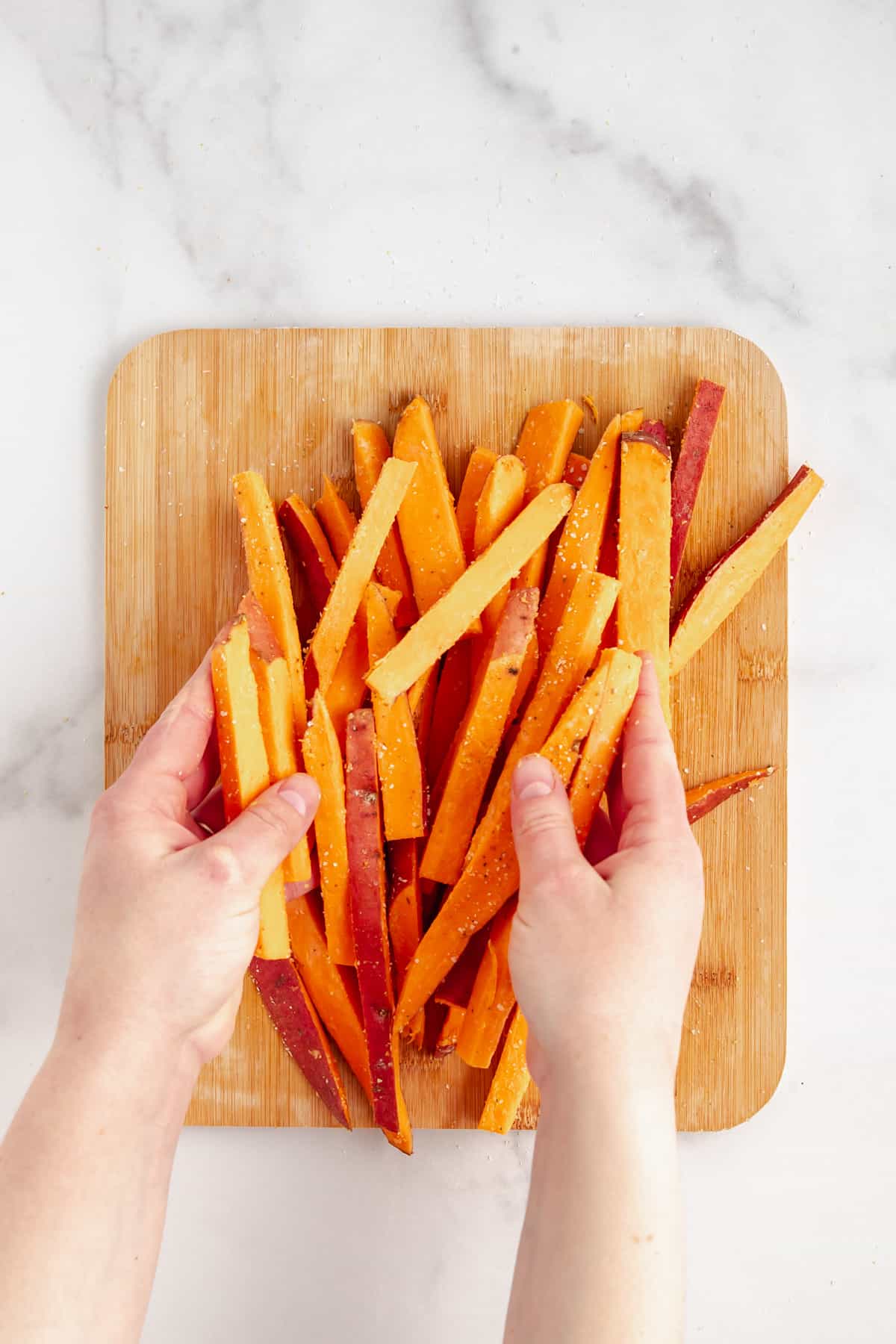 Sweet potato fries tossing with seasonings on a cutting board.