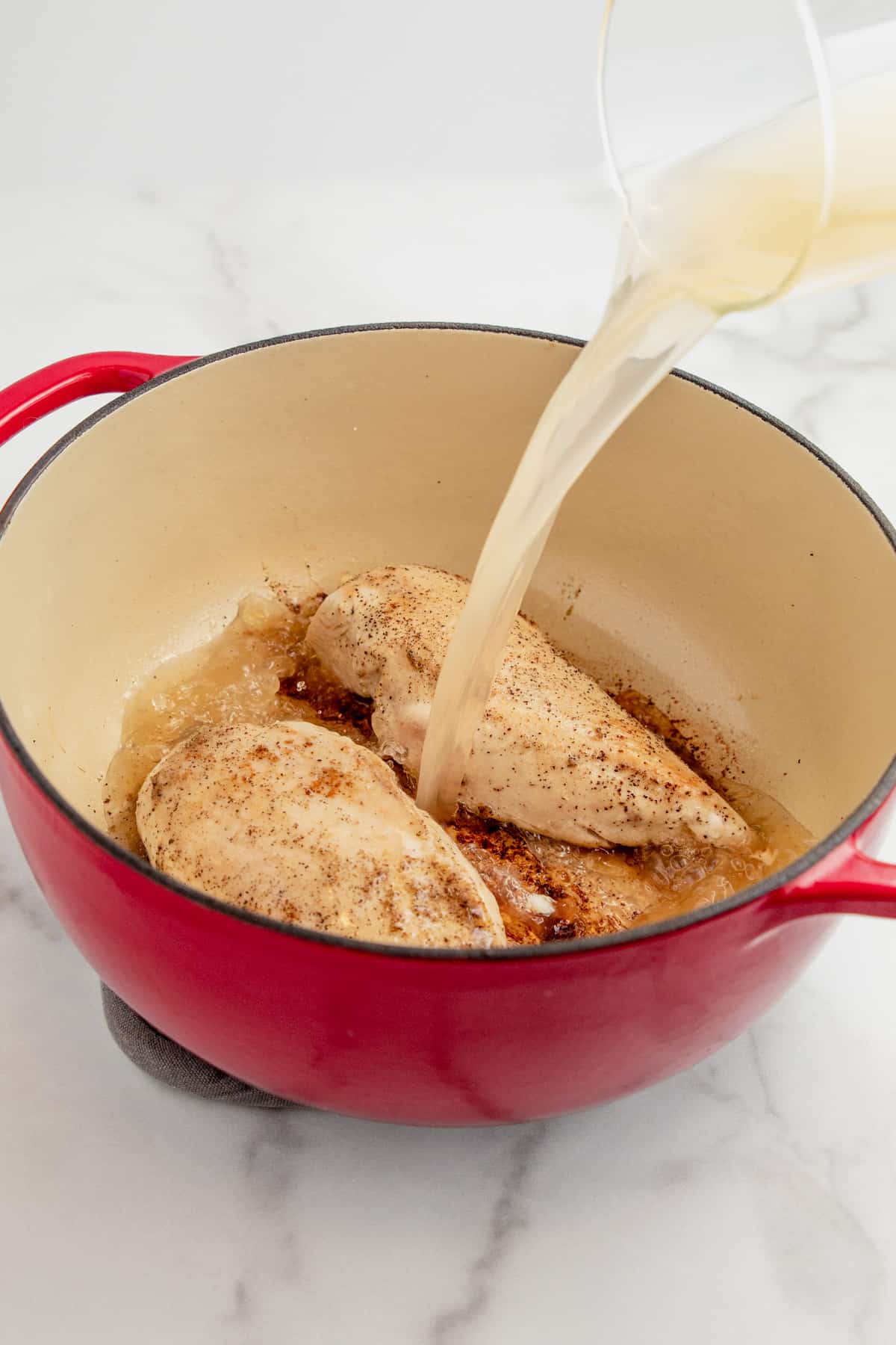 Pouring chicken broth over chicken breasts in a dutch oven.