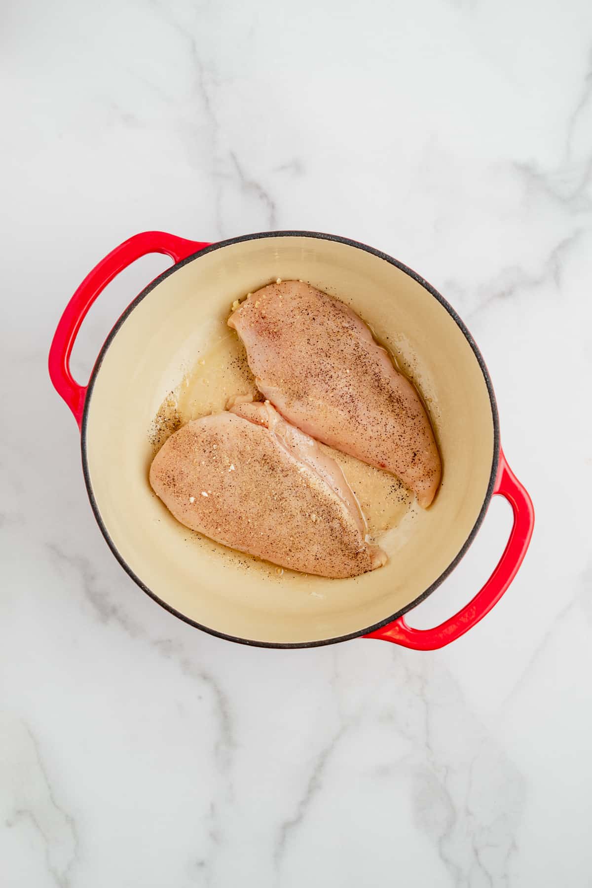 Two chicken breasts browning in a dutch oven.
