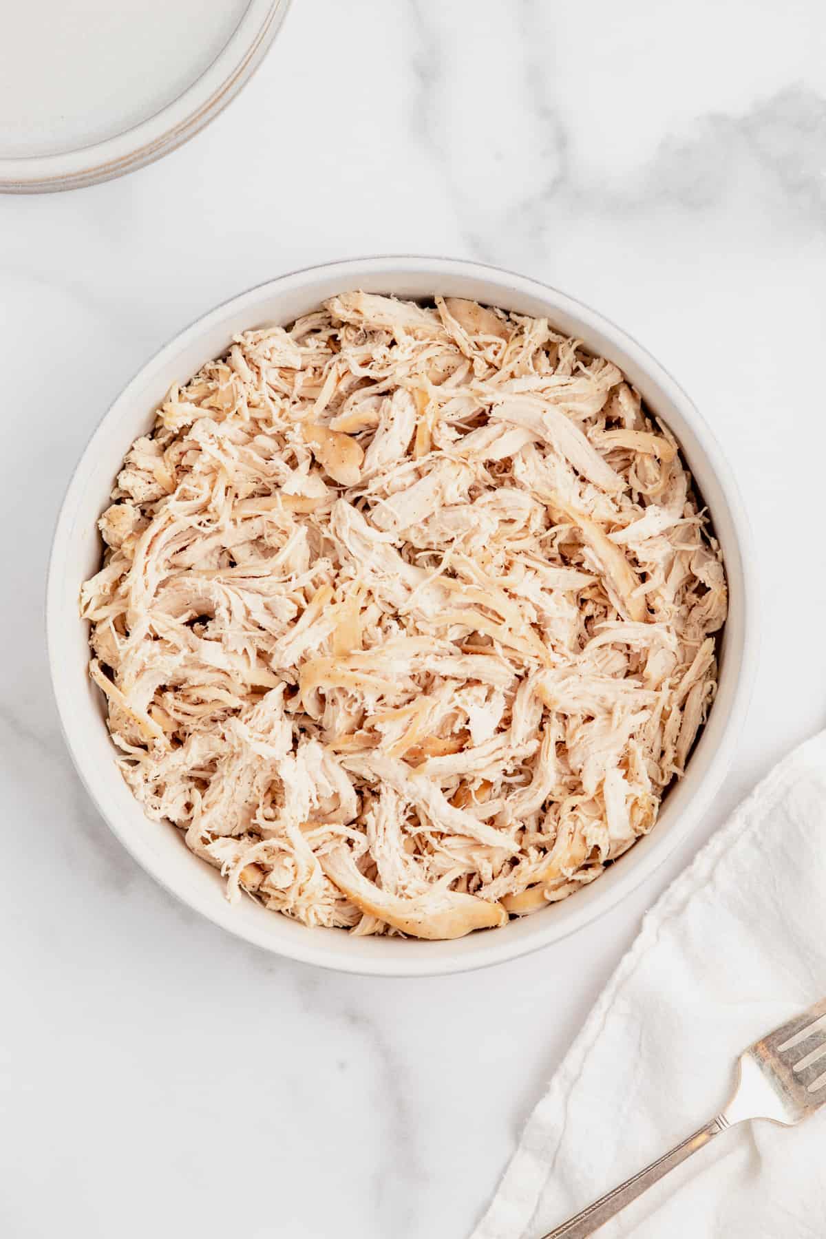 Shredded chicken in a bowl next to a fork.