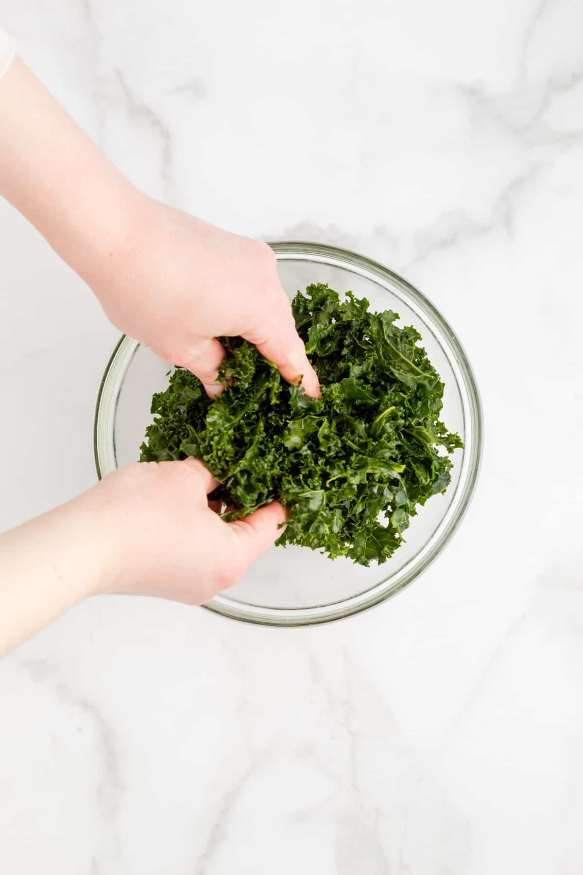 Massaging chopped kale in a bowl.