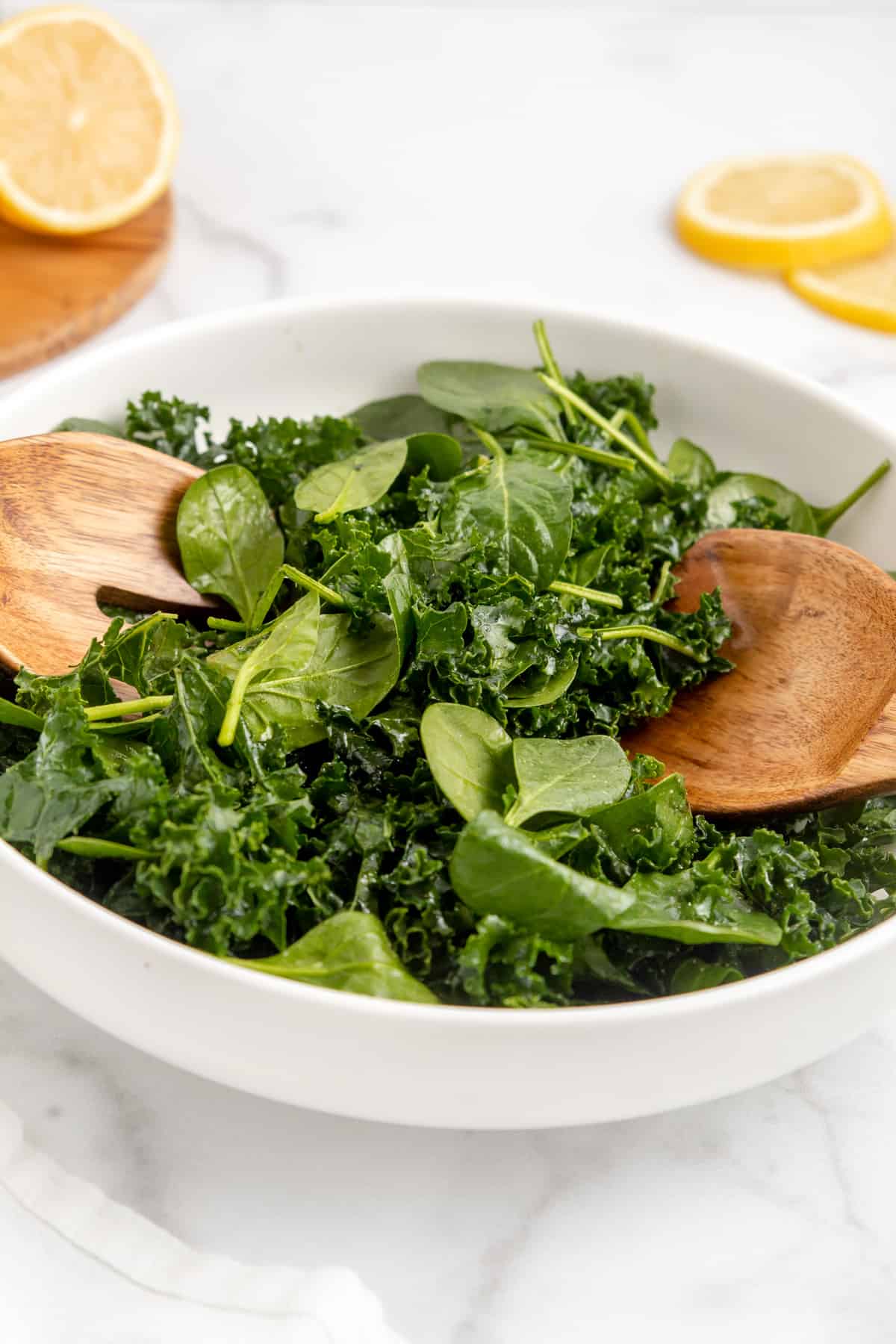 Kale and spinach salad in a bowl topped with a lemon vinaigrette with two wooden serving spoons.