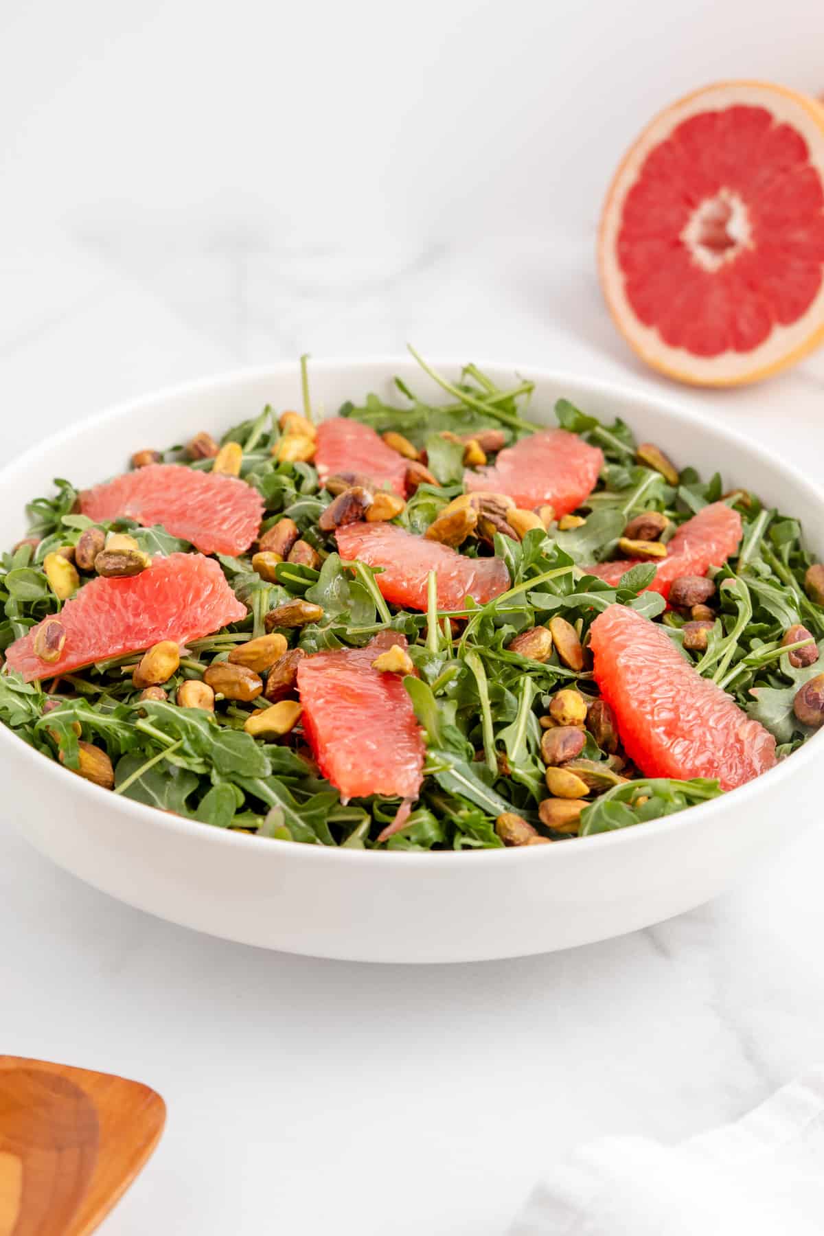 Side view of a grapefruit and arugula salad topped with dressing and pistachios.