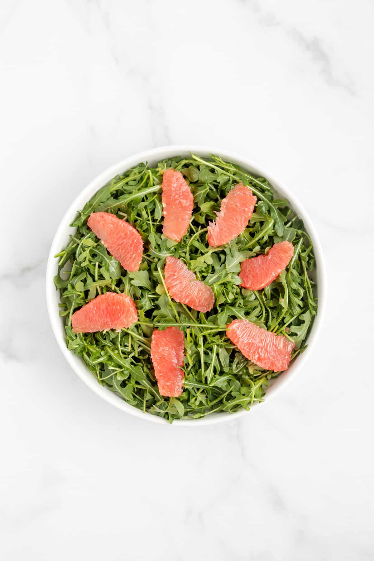 A bed of arugula in a bowl topped with grapefruit segments.