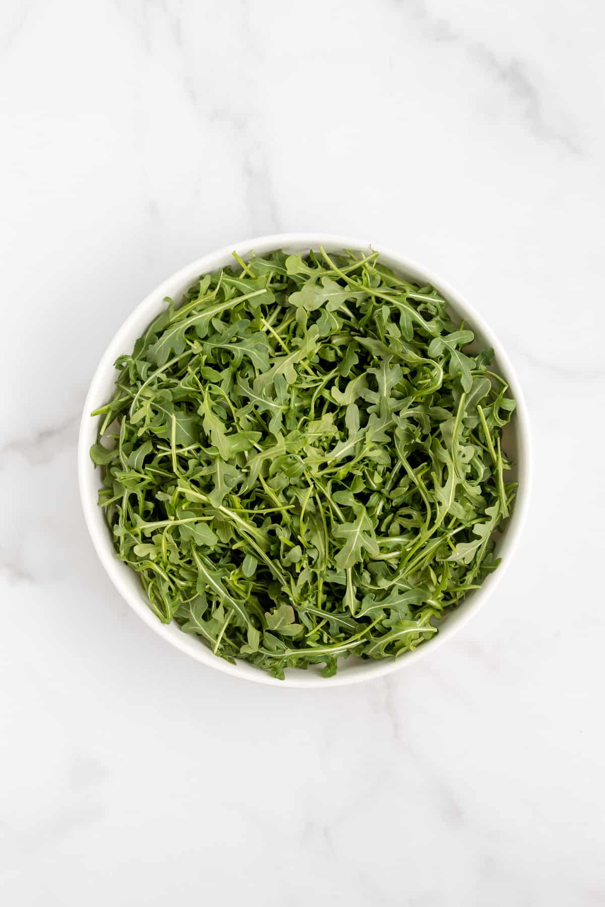 A bed of arugula in a large white bowl.