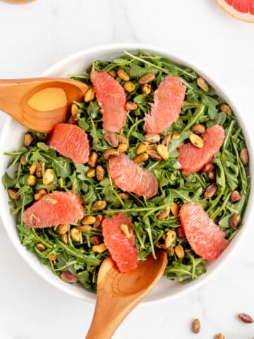 Grapefruit and arugula salad topped with dressing and pistachios.