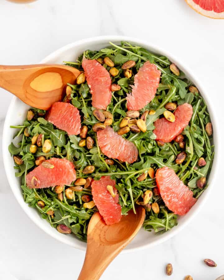 Grapefruit and arugula salad topped with dressing and pistachios.