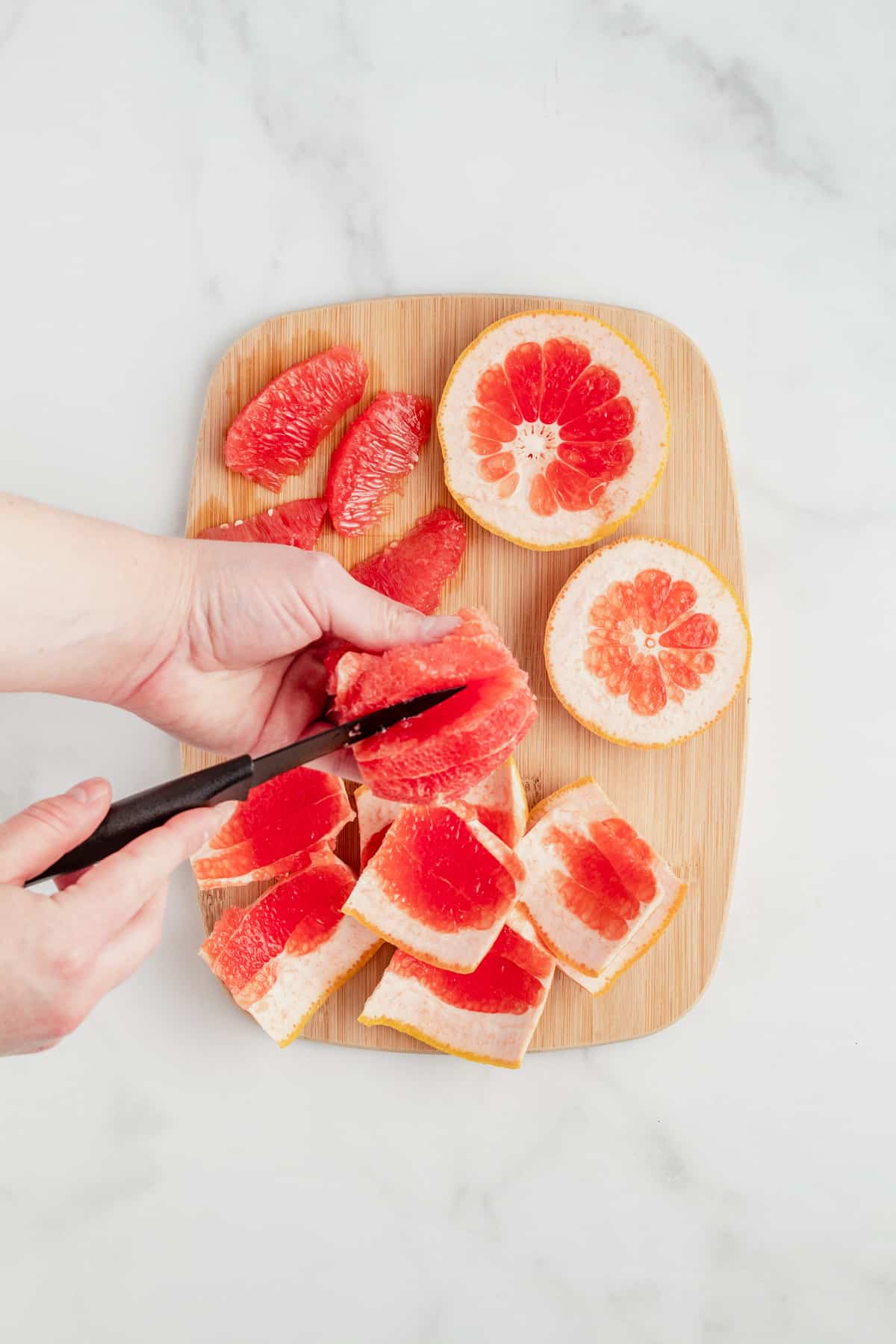 Cutting grapefruit into segments on a cutting board.