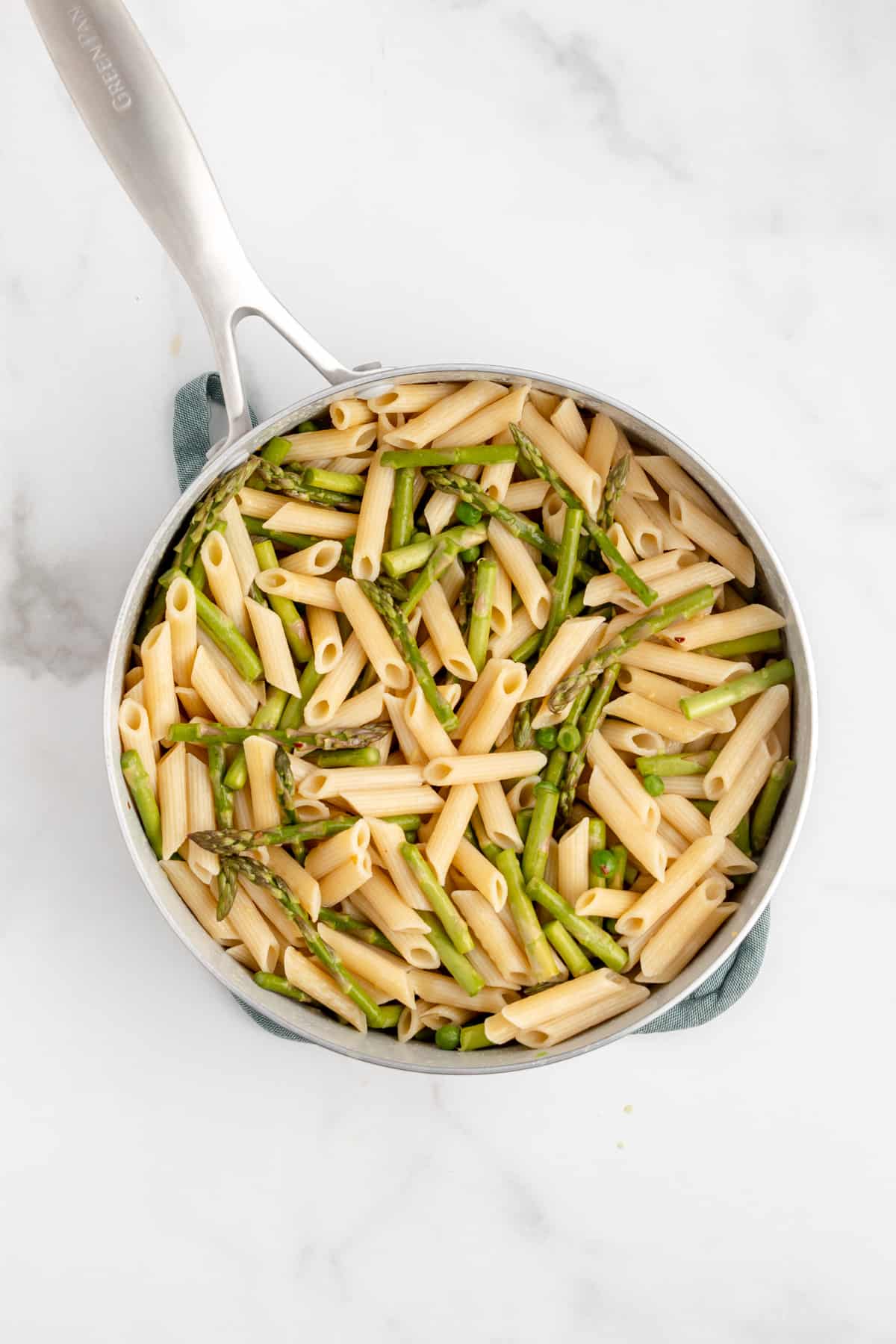 Cooked pasta in a pan with asparagus, peas, and butter sauce.