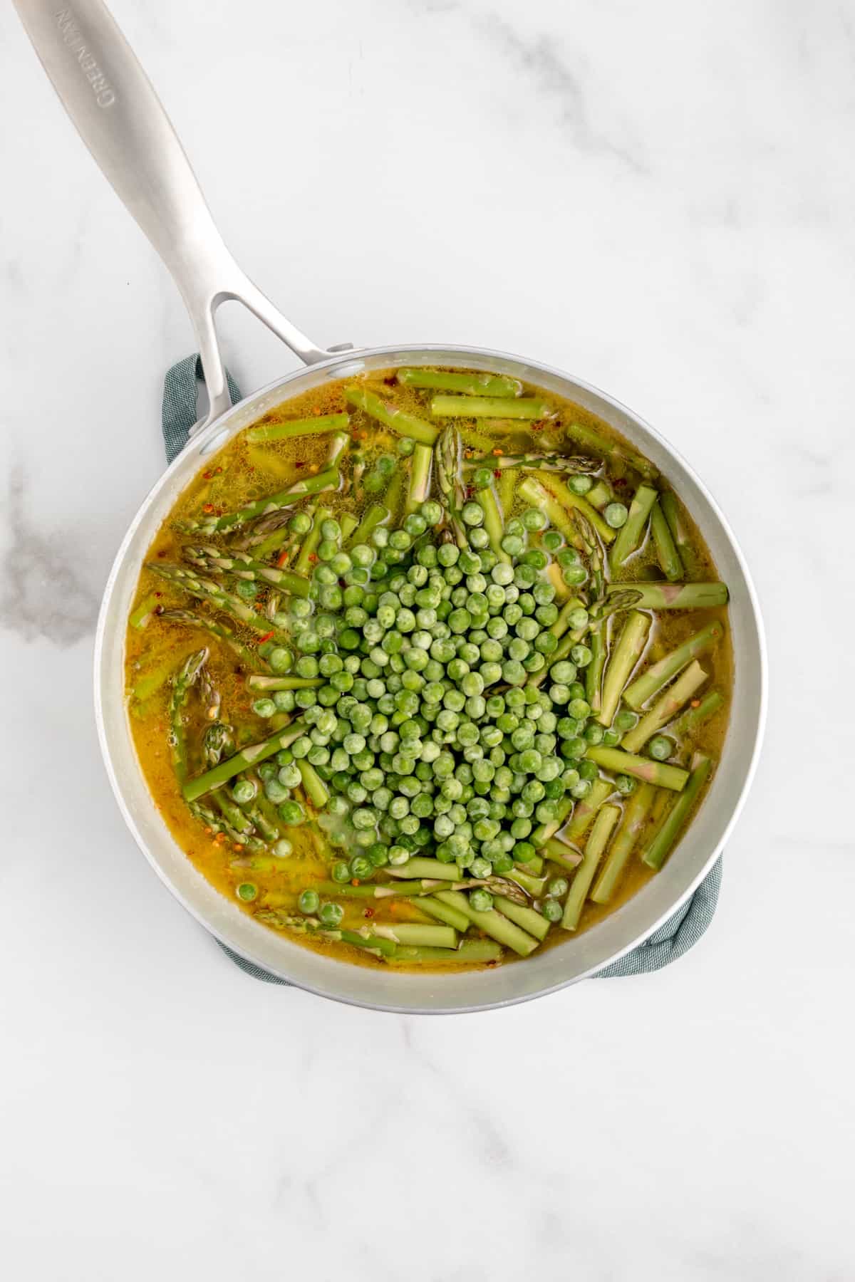 Butter, asparagus, peas and pasta water in a saucepan.