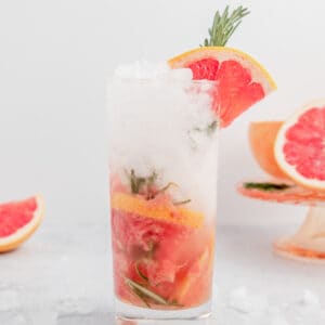 Grapefruit mojito with rosemary in a tall glass garnished with a fresh sprig of rosemary and a grapefruit wedge.
