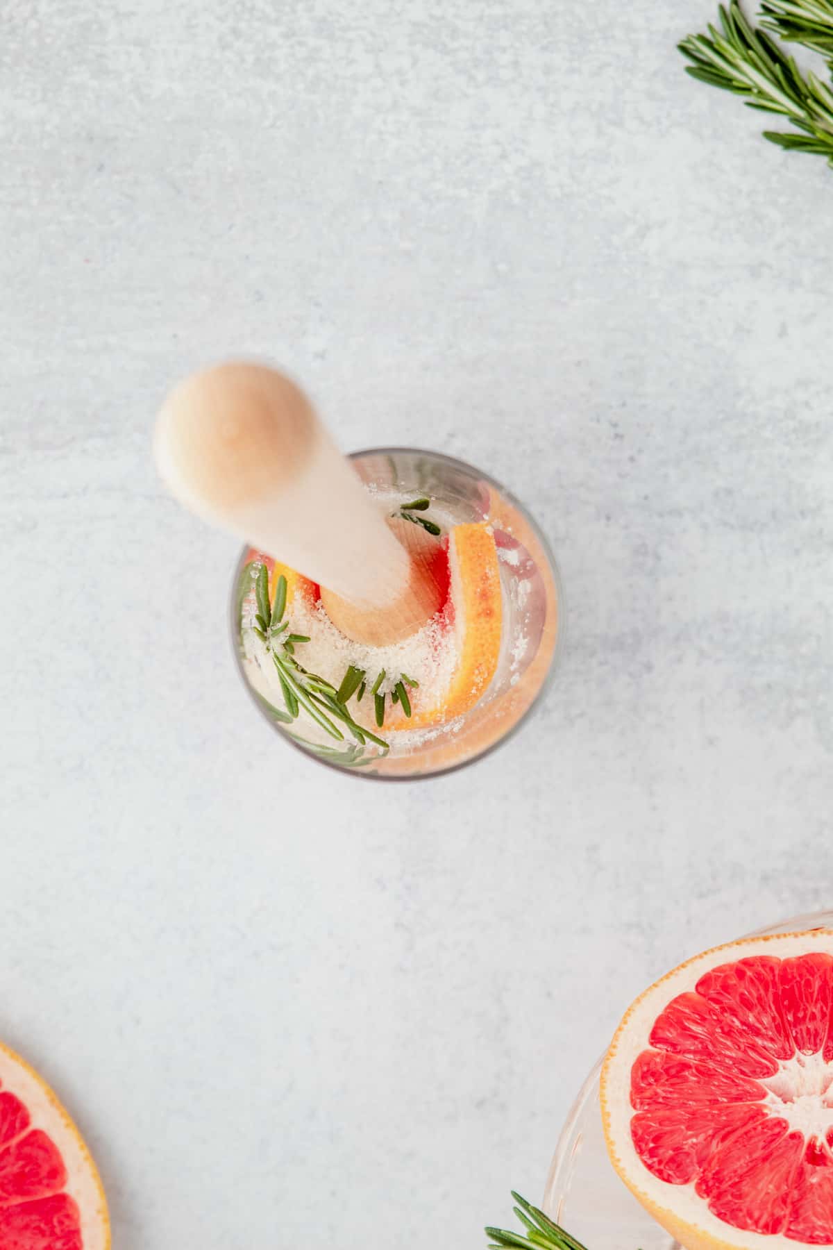 Grapefruit, sugar, and rosemary in a glass with a muddler.