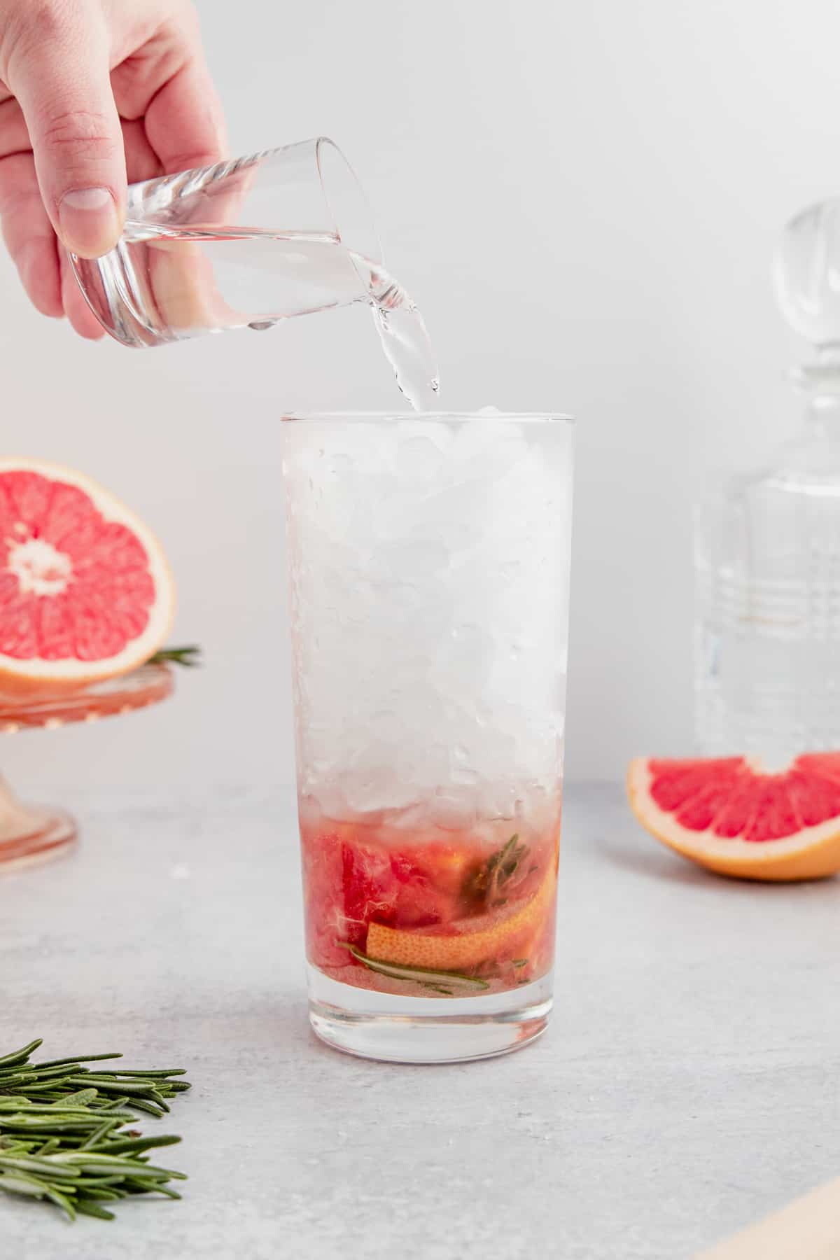 Pouring rum into a glass with muddled rosemary and grapefruit.