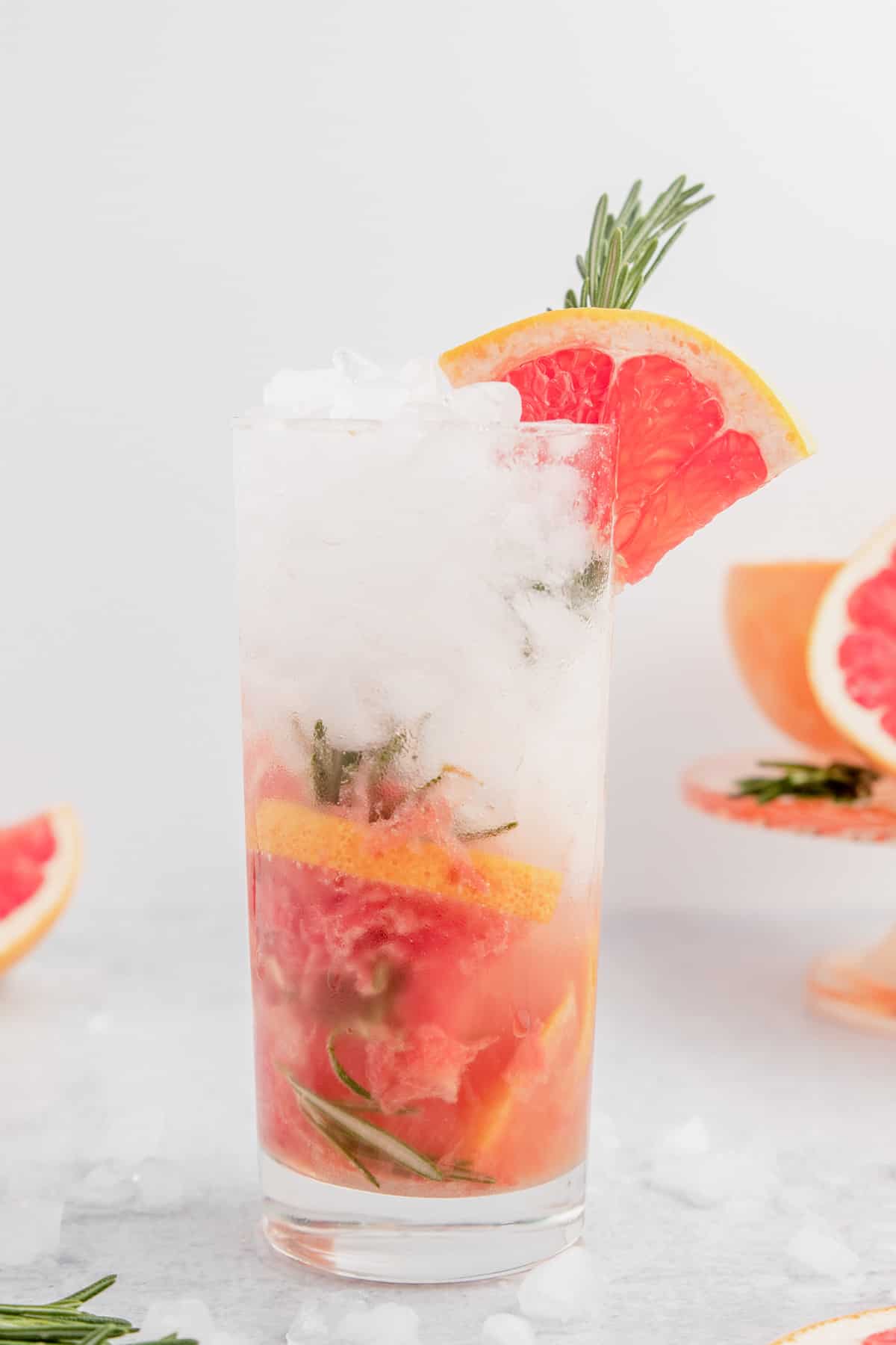 Grapefruit mojito with rosemary in a tall glass garnished with a fresh sprig of rosemary and a grapefruit wedge.