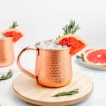 An icy copper mug full of Moscow mule with a grapefruit wedge and rosemary sprig.