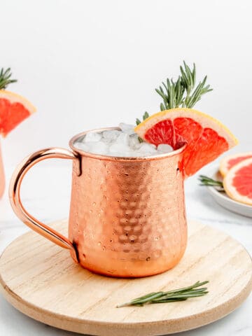 An icy copper mug full of Moscow mule with a grapefruit wedge and rosemary sprig.