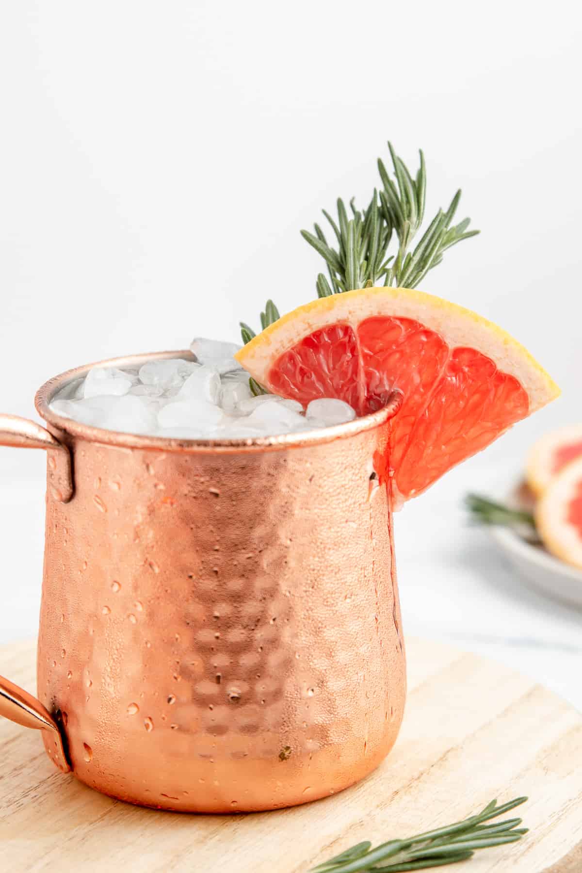 A copper mug full of Moscow mule with a grapefruit wedge and fresh rosemary sprig.