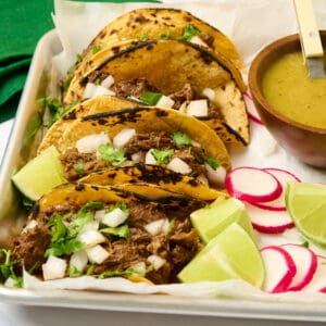 Featured image of four barbacoa street tacos on a platter topped with onion and cilantro.