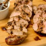 Sliced dutch oven pork tenderloin topped with gravy on a cutting board.