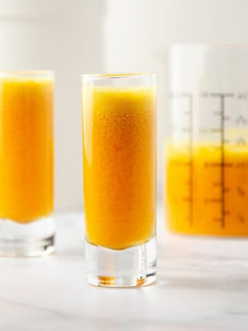 A featured image of two ginger turmeric shots with a measuring cup of the extra juice in the back.