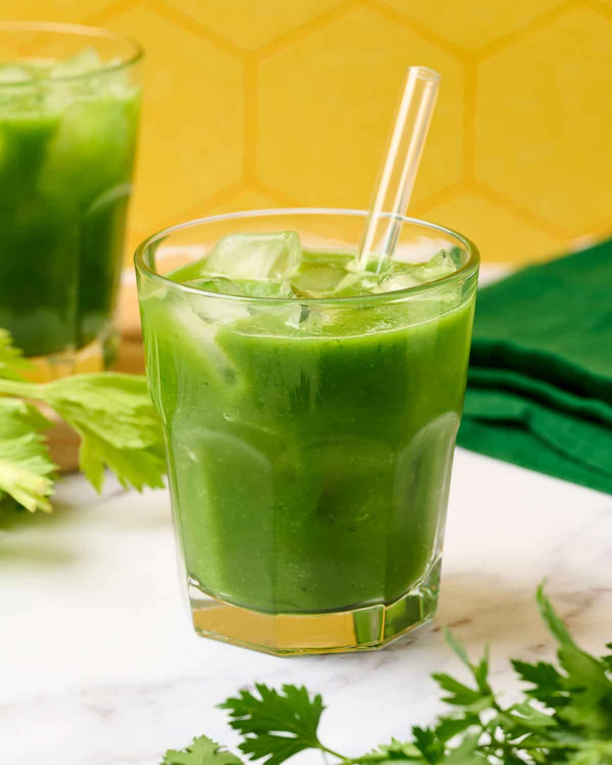 A glass of green goddess juice with apple, celery, and cucumber with a straw.