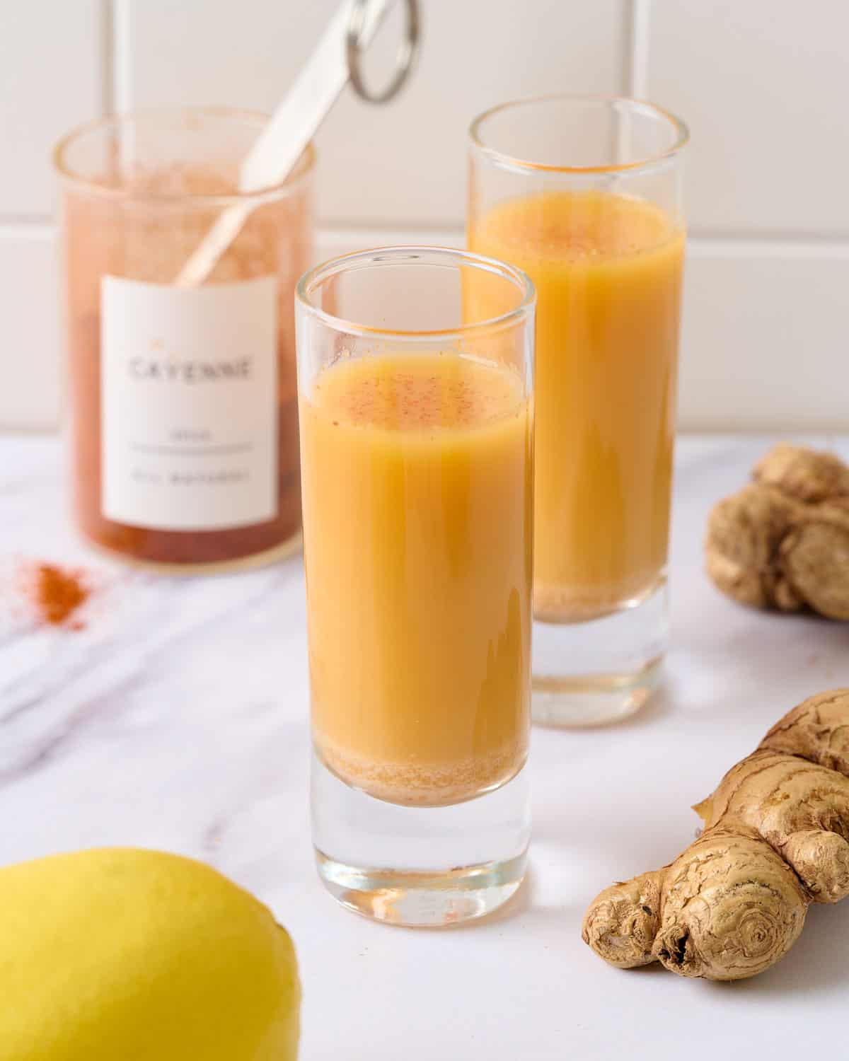 A close up image of two lemon ginger cayenne shots served in shot glasses.