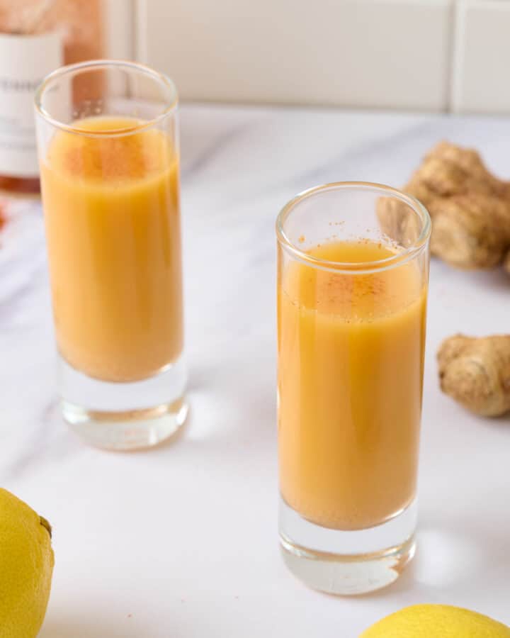 A featured image of two lemon ginger cayenne shots in two shot glasses.