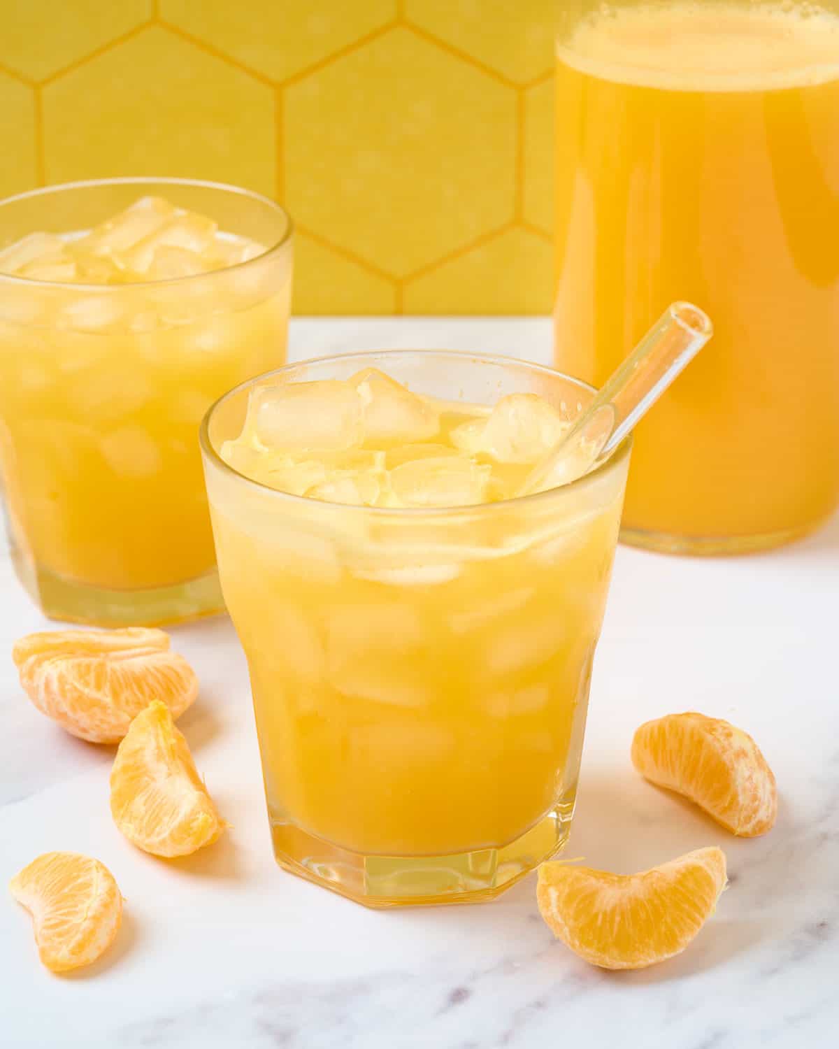 Finished mandarin juice in a large glass with a straw with a carafe of juice to the side.