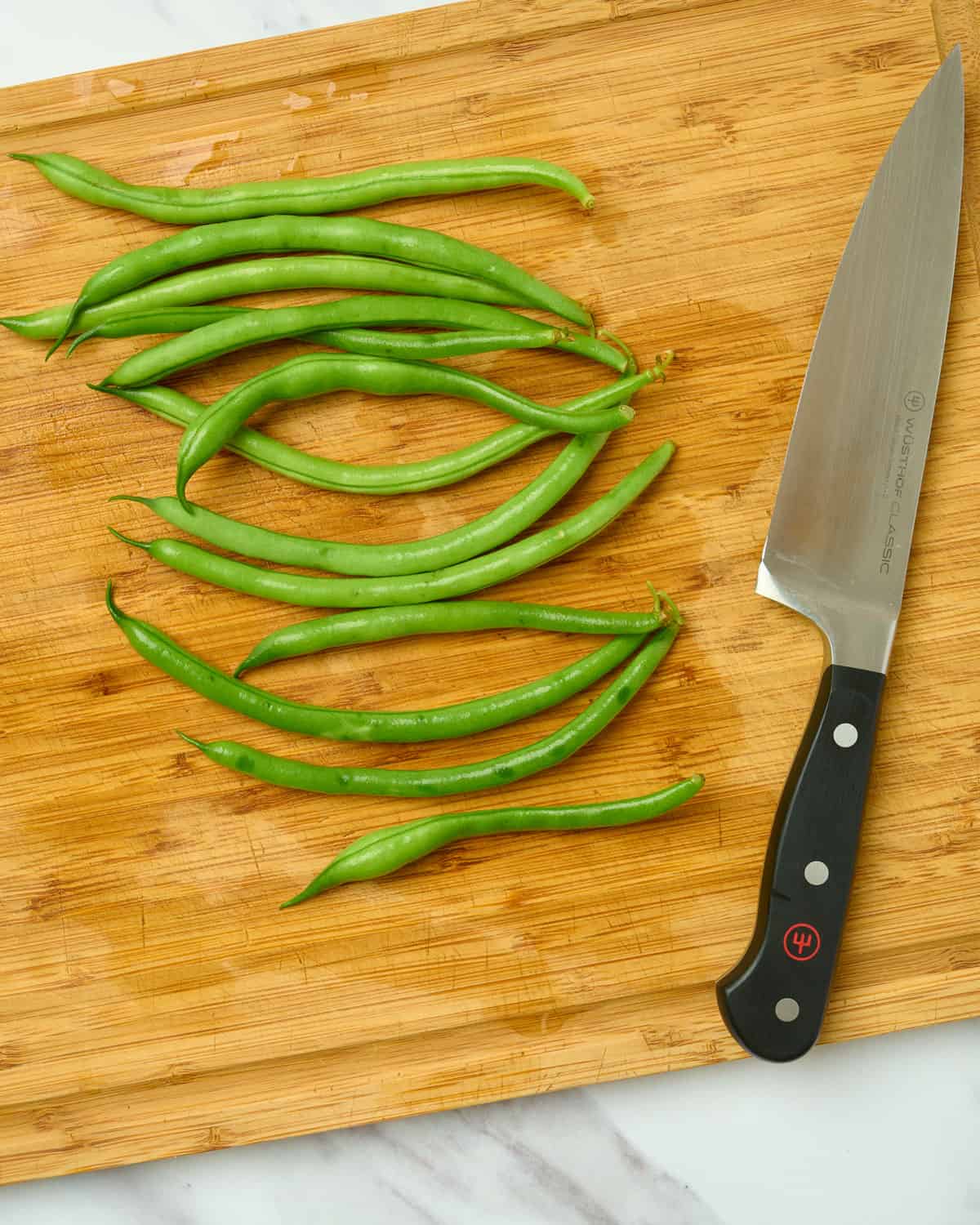 Green beans on a cutting board with a knife.