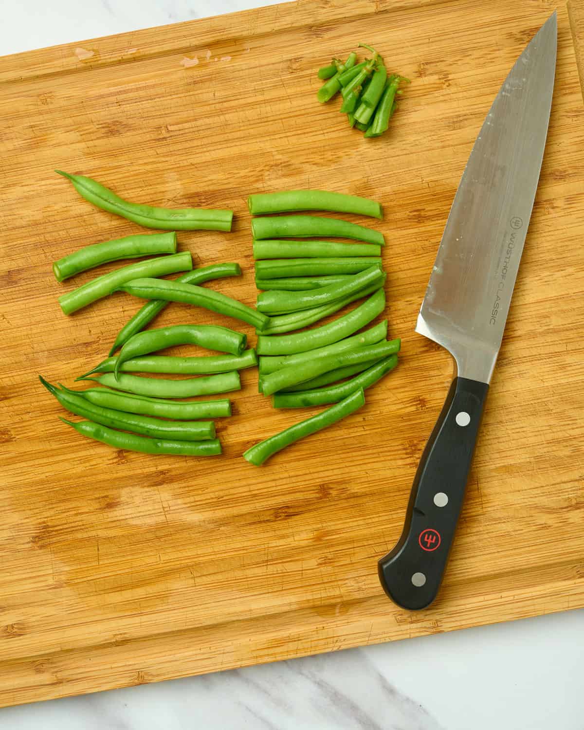 Green beans on a cutting board with stem ends trimmed off and cut in half.