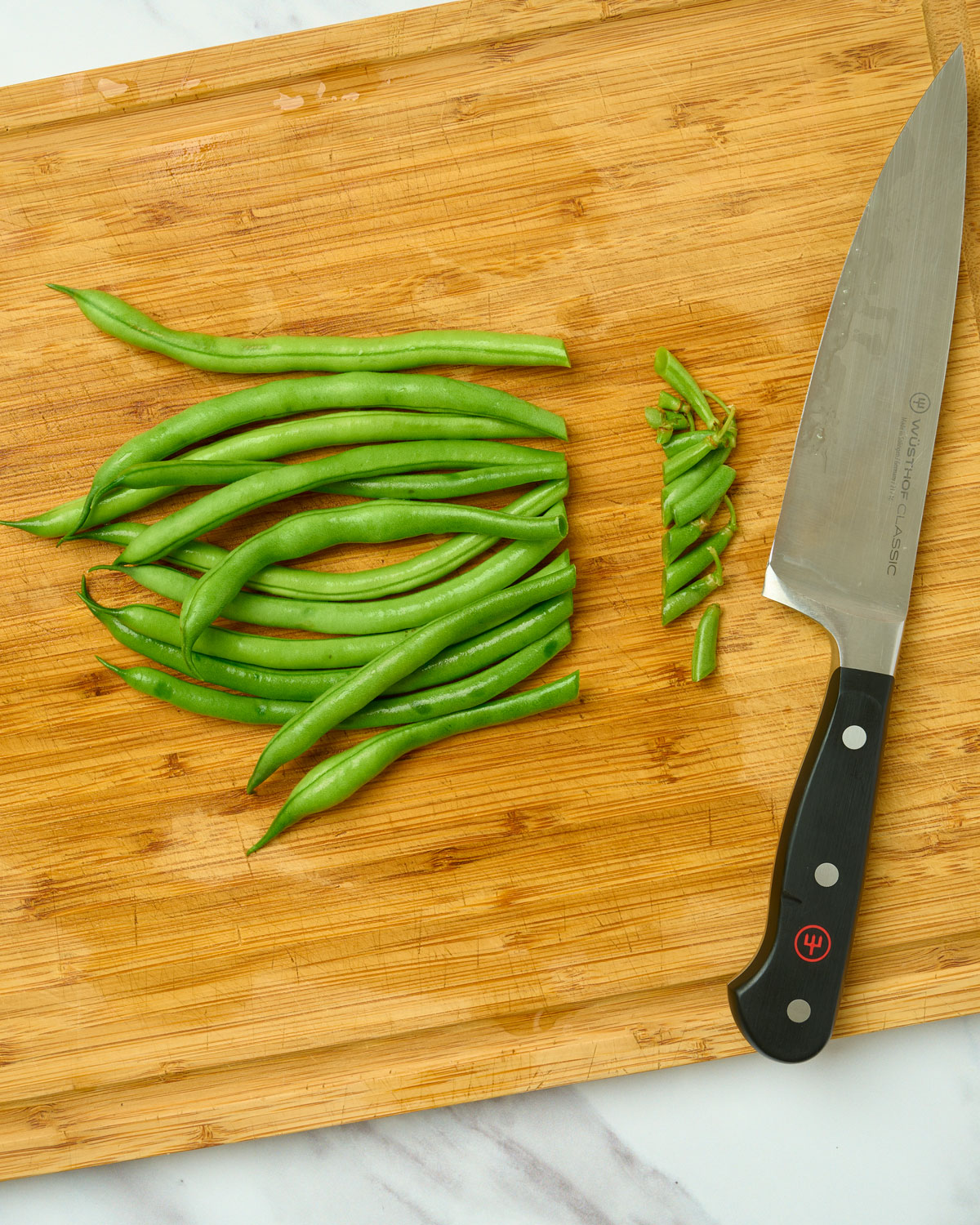 Green beans on a cutting board with stem ends trimmed off.