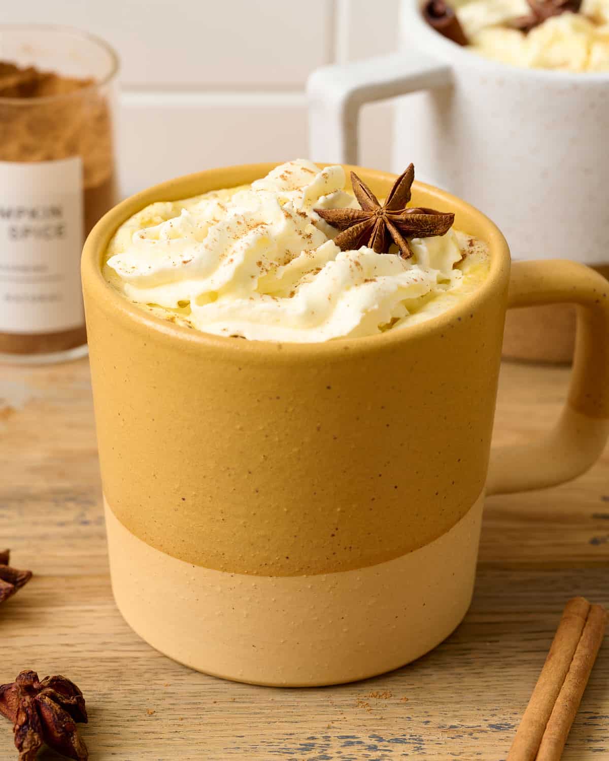 A yellow mug of pumpkin chai latte with coconut whipped cream on top.