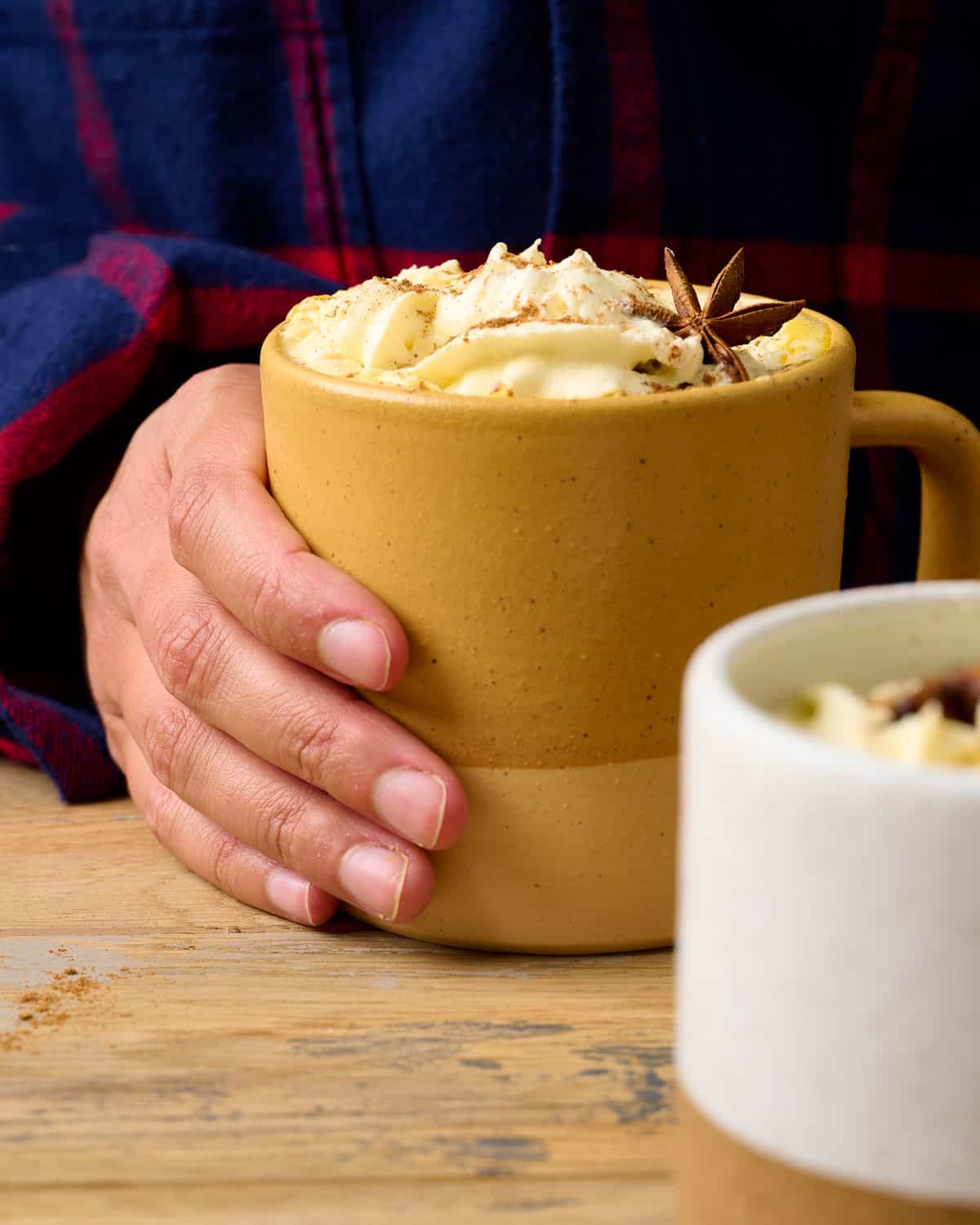 A hand holding a yellow mug filled with a pumpkin chai latte.