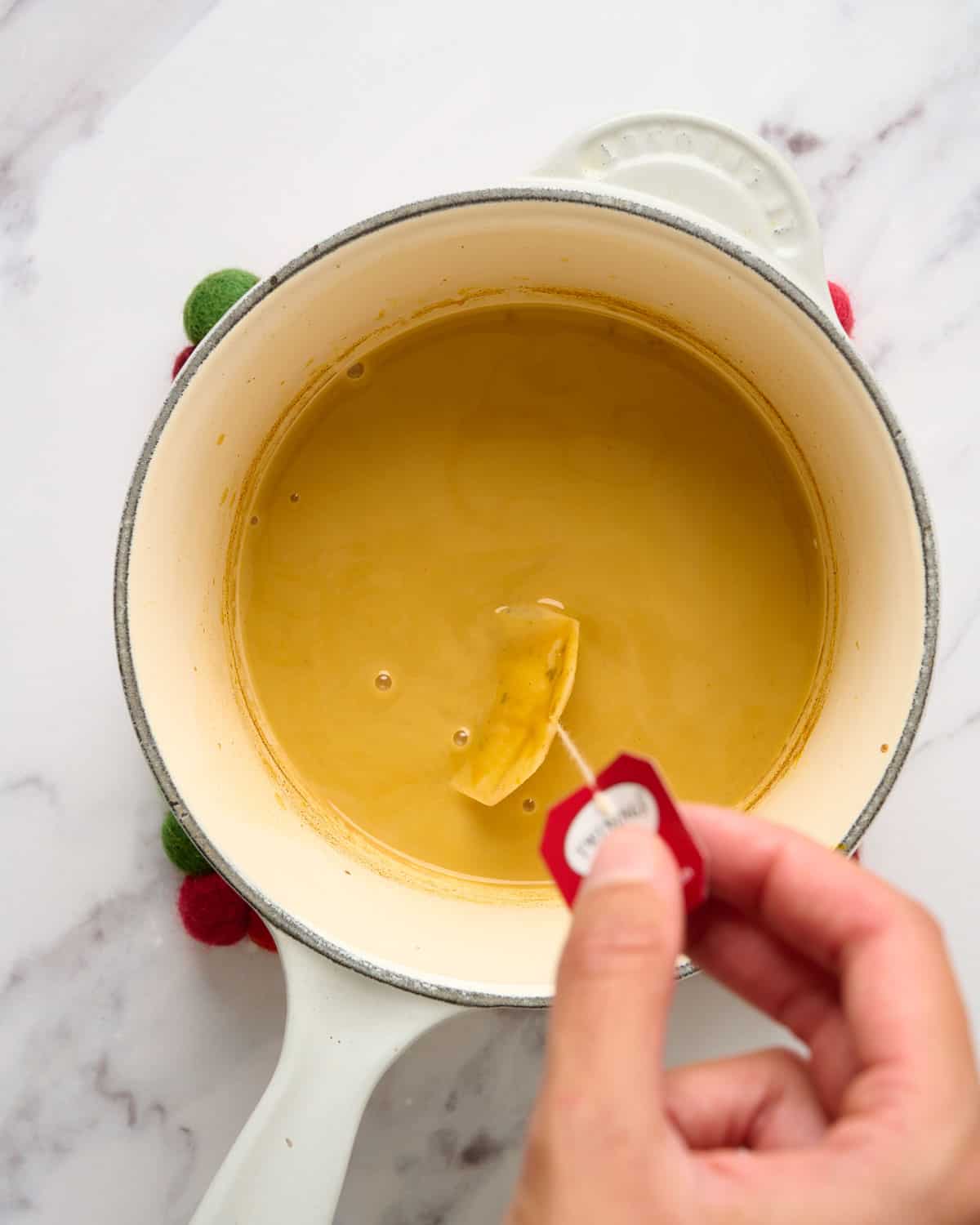 The process of adding a tea bag into a pumpkin-oat milk mixture to make a pumpkin chai latte.