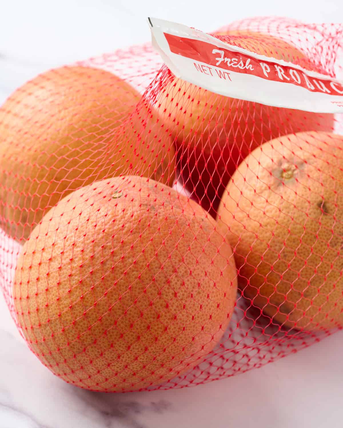 A mesh bag of fresh grapefruit on the couter.
