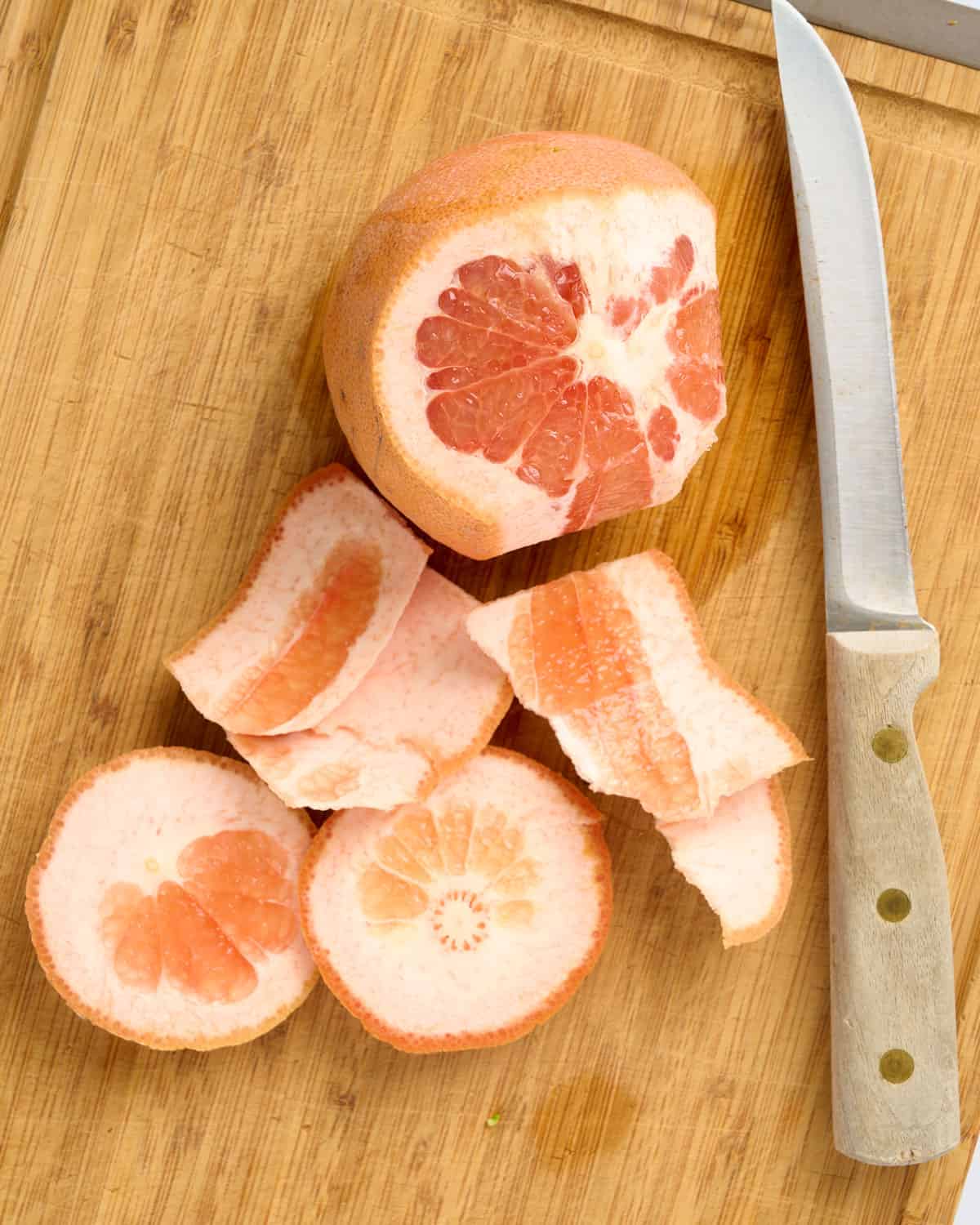 A grapefruit with some of the peel removed on a cutting board.