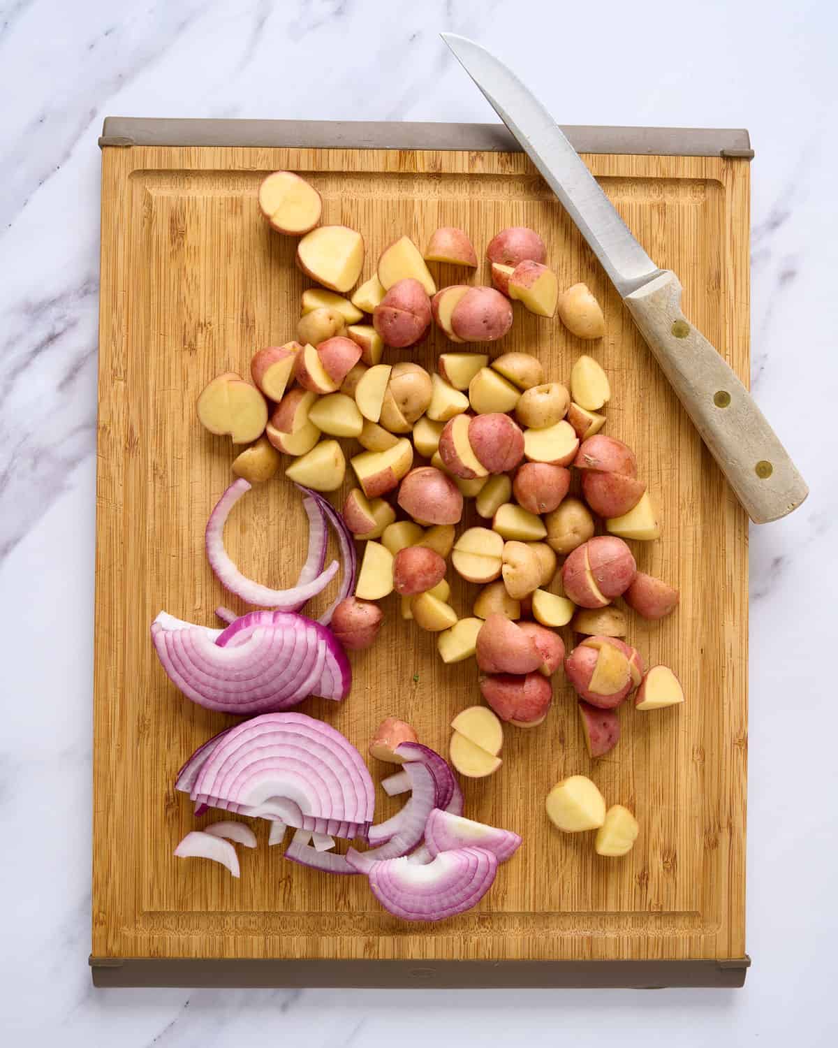 Sliced onions and potatoes on a cutting board.