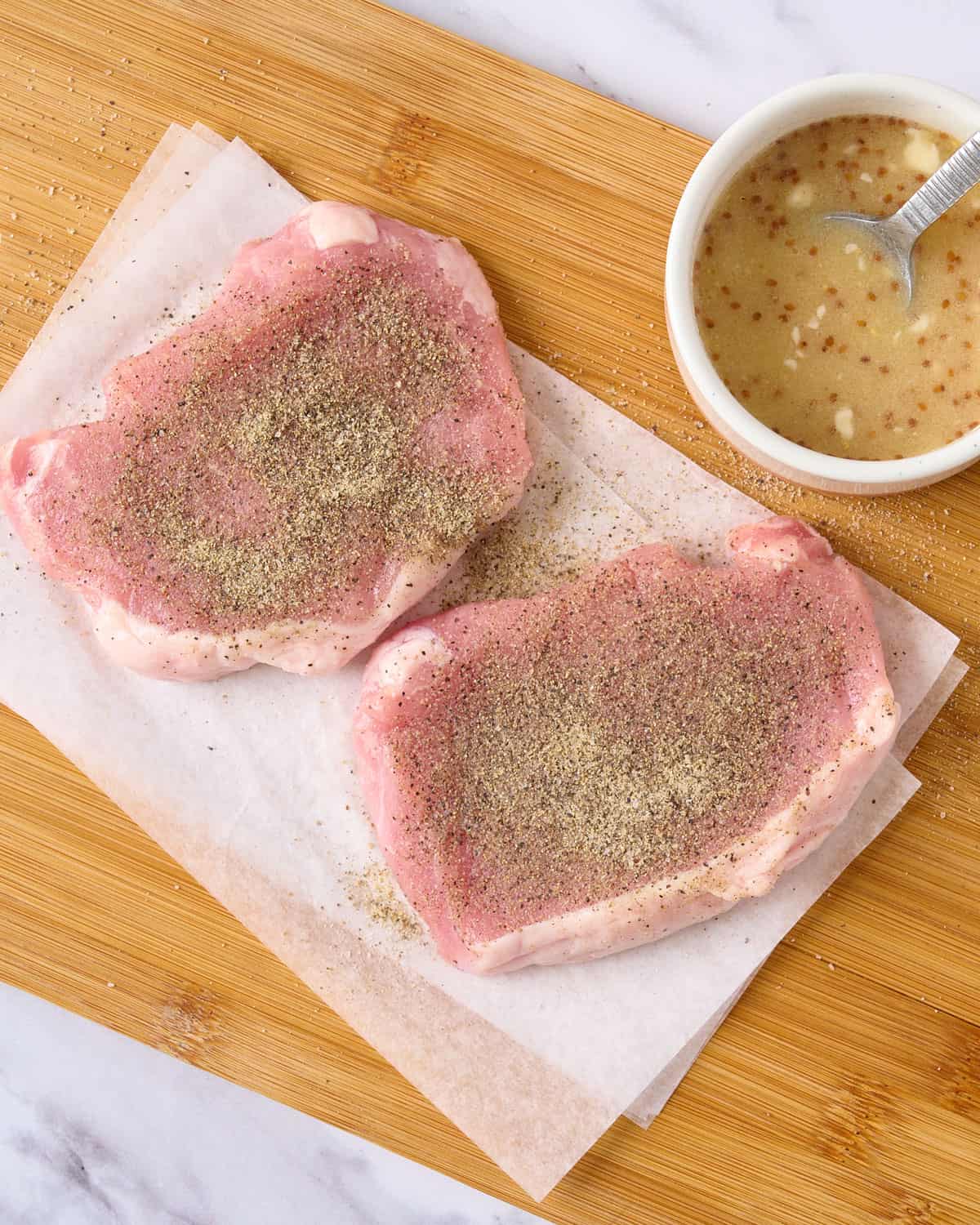 Seasoned pork chops on a cutting board.