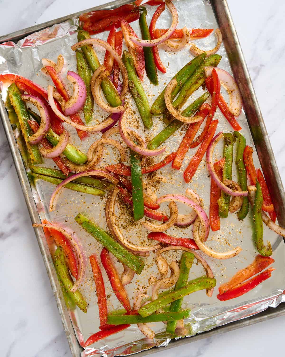 Halloumi fajitas raw bell peppers and onion on sheet tray with seasoning mix.