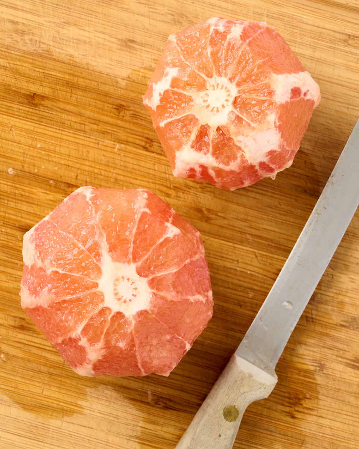 Peels removed from two grapefruits on a cutting board with a knife.