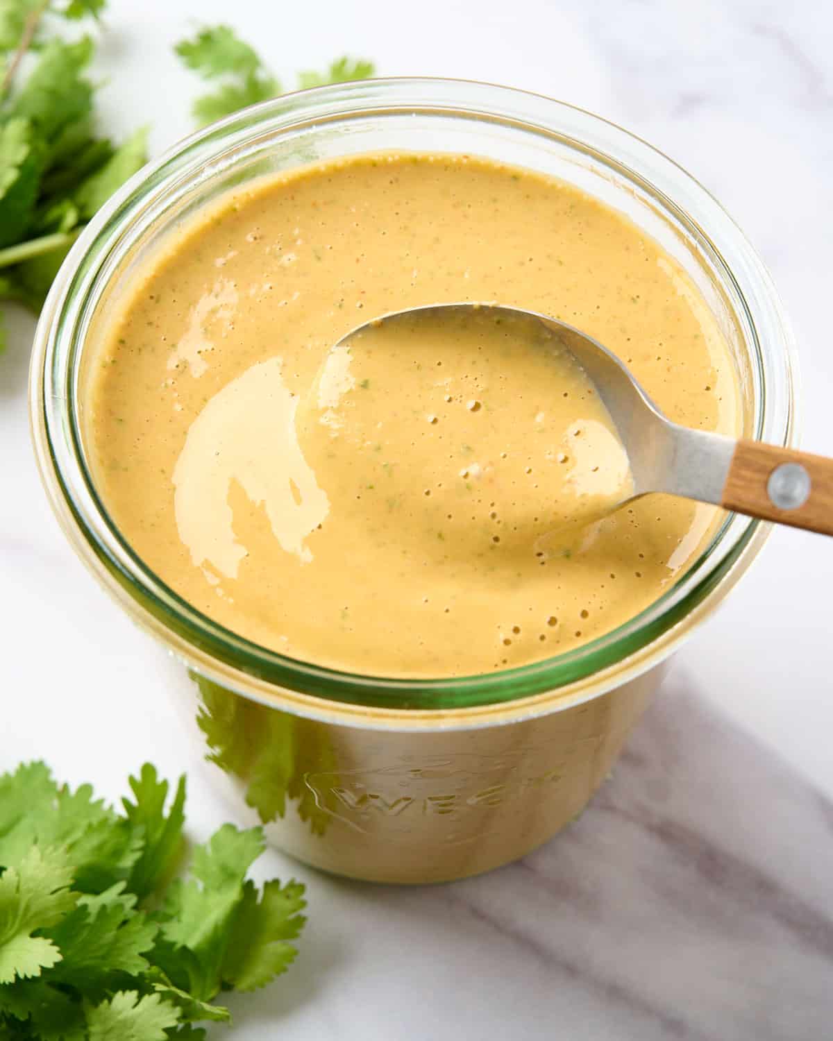 A large jar of spicy cashew dressing with a spoon drizzling the dressing.