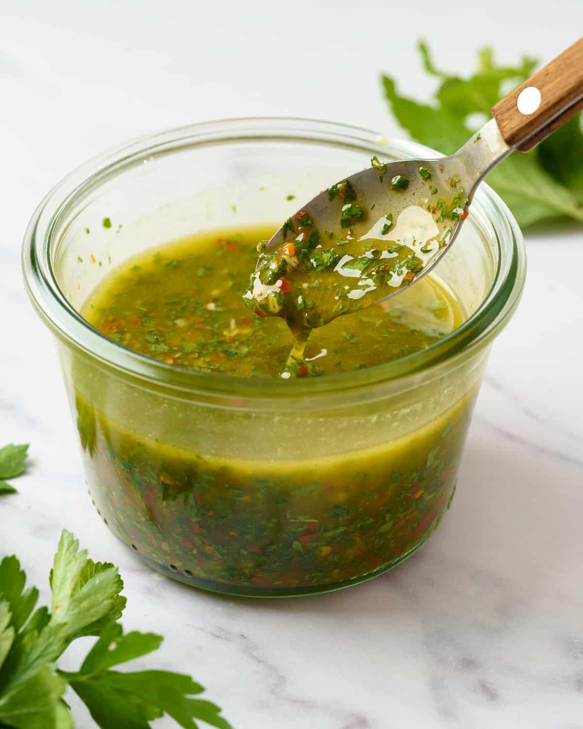 Spicy chimichurri in airtight container with spoonful dripping out.