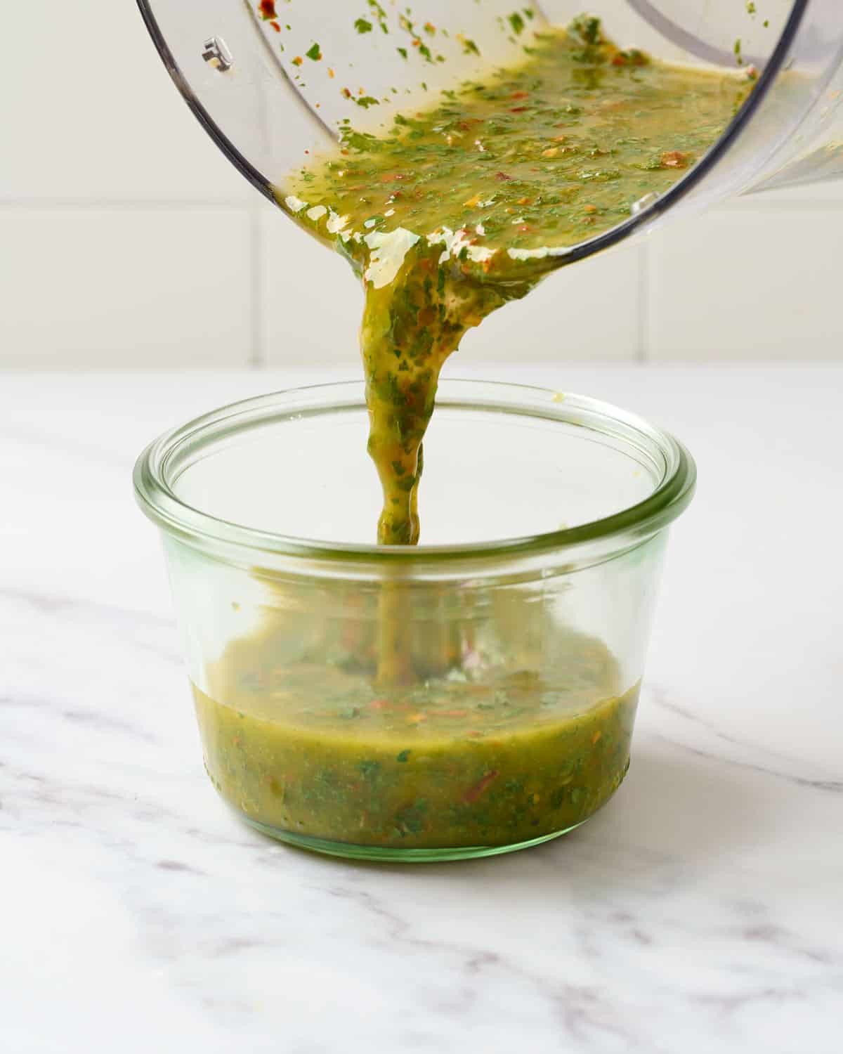 Pouring spicy chimichurri into airtight container.