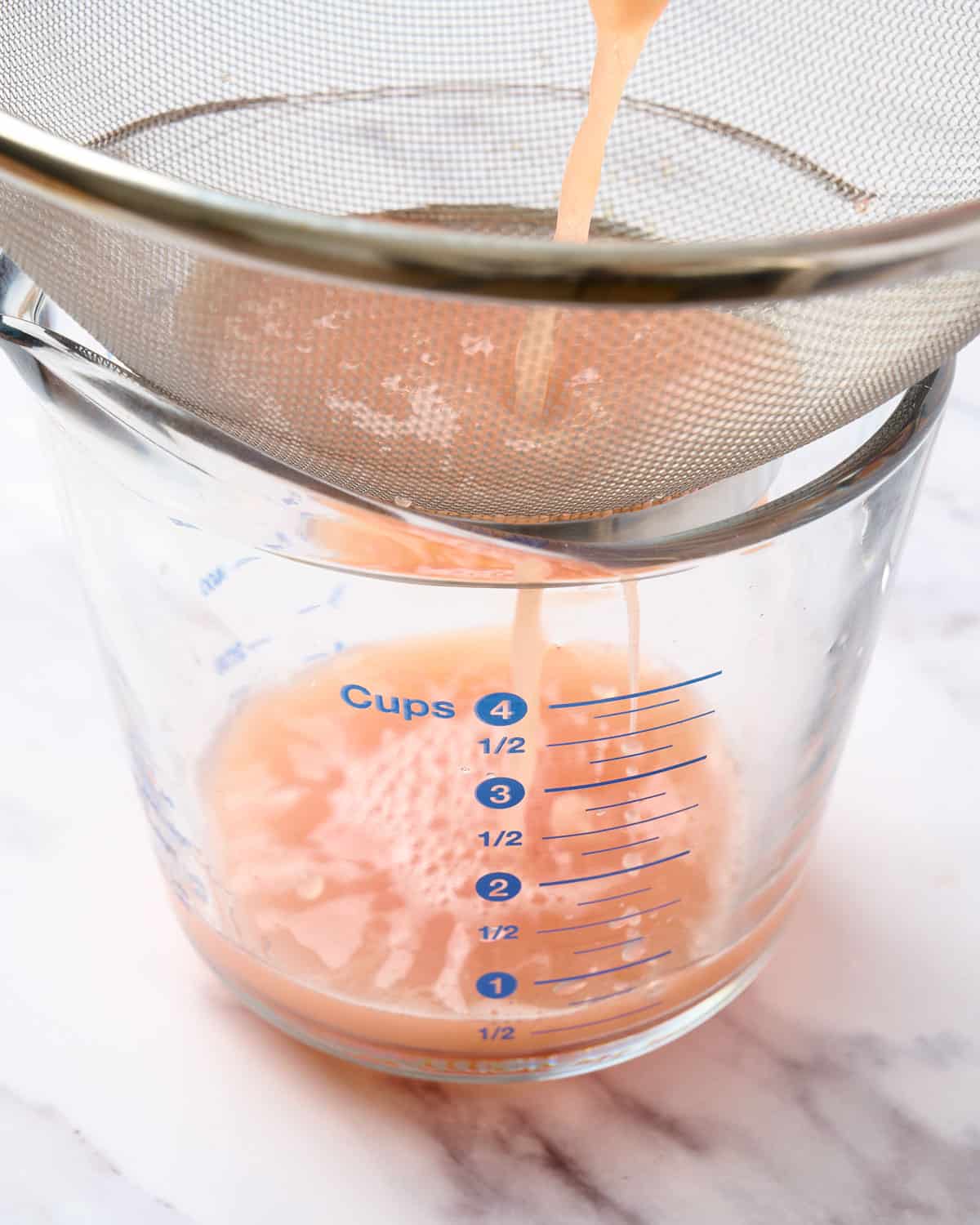 Straining freshly squeezed grapefruit juice with a fine mesh strainer.
