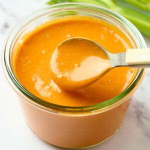 A spoonful of buffalo sauce pouring into a jar.