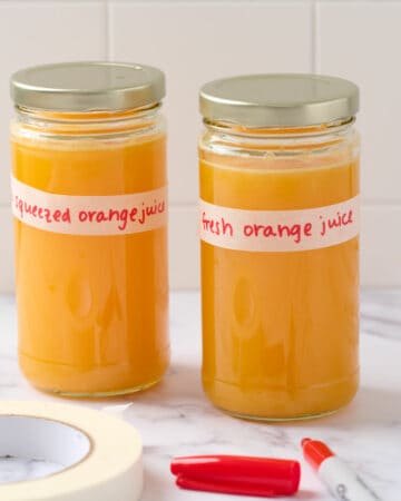 A featured image showing two glass jars filled with fresh orange juice and labeled to demonstrate how to properly label for the fridge.