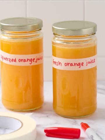 A featured image showing two glass jars filled with fresh orange juice and labeled to demonstrate how to properly label for the fridge.