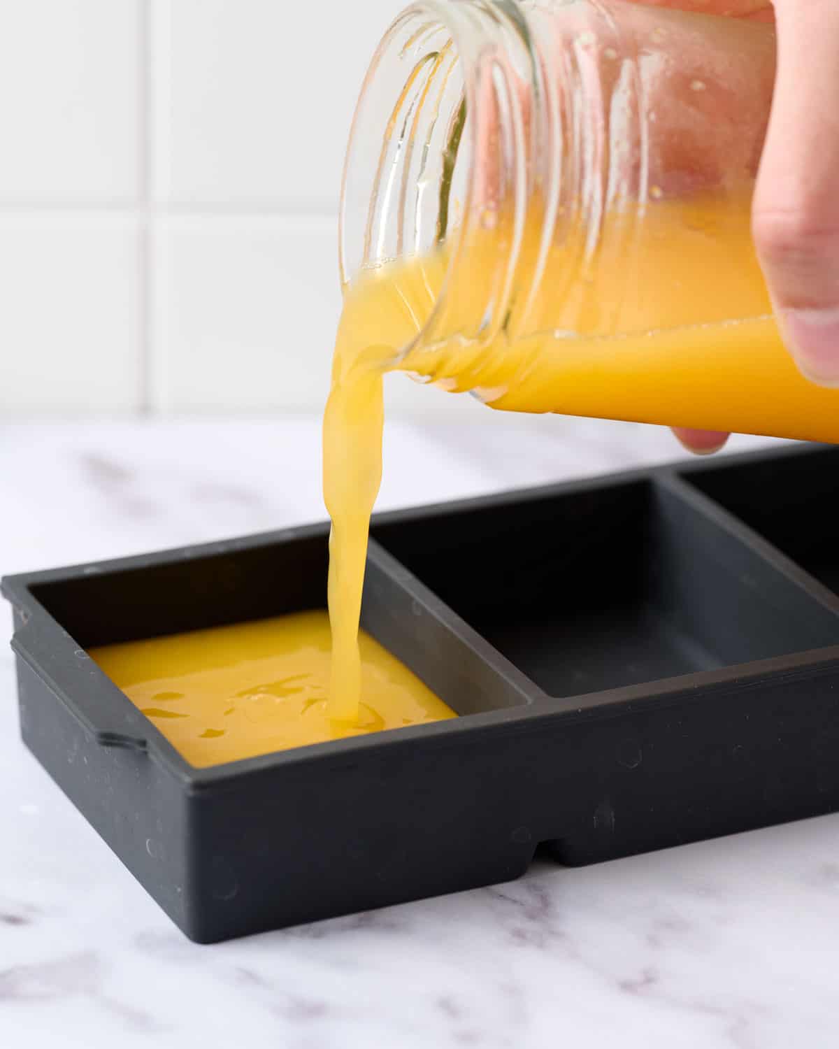 Pouring fresh orange juice into ice cubes for freezing.