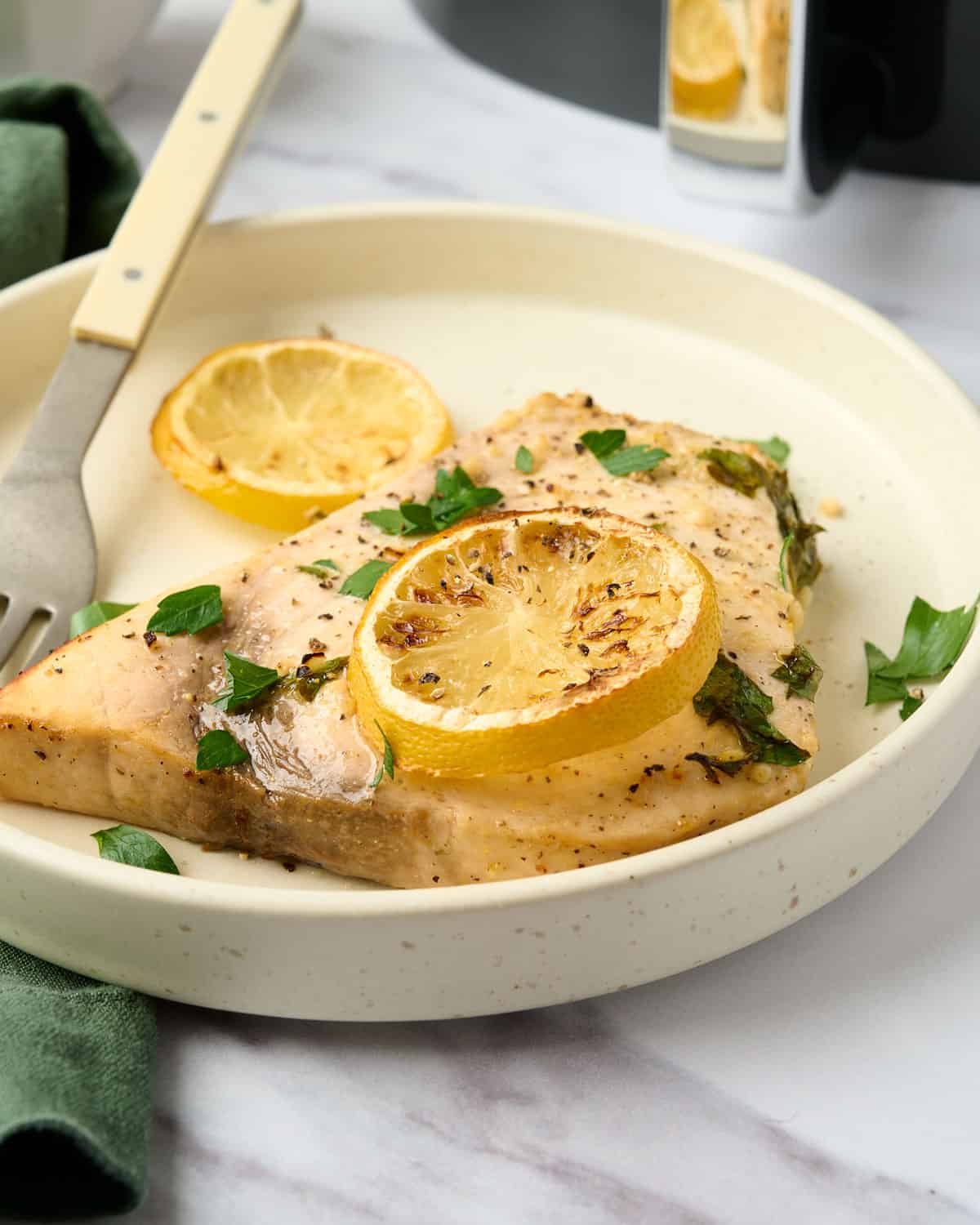 Lemon pepper swordfish with a lemon slice on a plate.